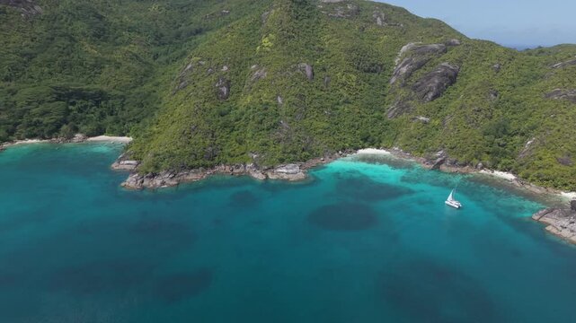 Drone footage of a luxury catamaran anchored in the vibrant turquoise waters of Anse Du Riz beach, surrounded by lush tropical hills and granite rocks and anse major beach in Mahe, Seychelles.