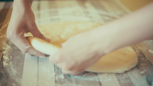 Close-up of baker hands stretching and shaping fresh yeast dough on a floured wooden table. Hand-shaping raw sweet pastry before rolling pin sequence for cinnamon rolls recipe, 4k.