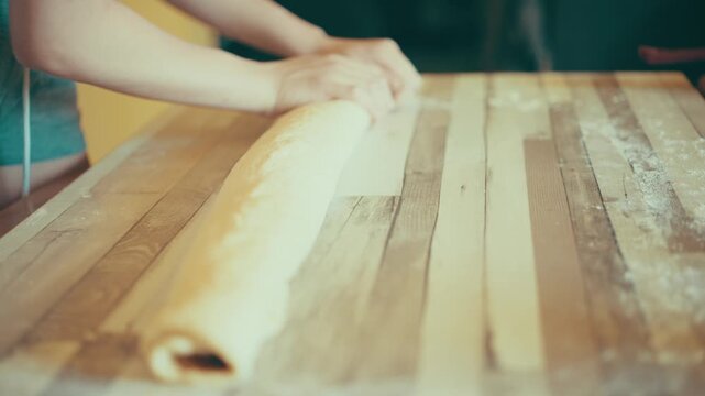 Close-up of baker hands shaping and tightening a long rolled cinnamon dough log on a floured wooden table. Adjusting raw sweet pastry roll before slicing sequence in the kitchen, 4k.