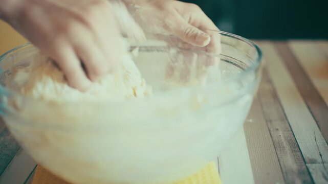 Close-up of baker hands mixing and kneading fresh yeast dough inside a glass bowl on a wooden table. Dynamic action of preparing homemade sweet pastry recipe from scratch in kitchen, 4k.