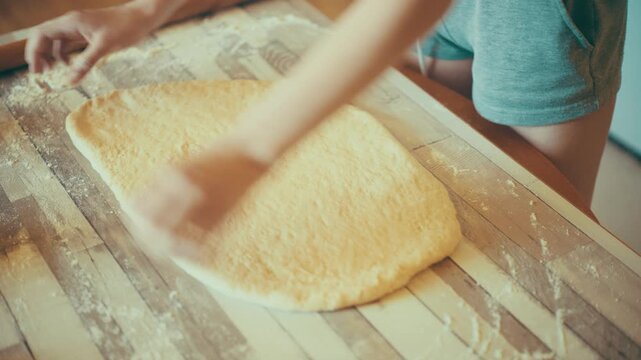 Close-up of baker hands stretching and shaping fresh yeast dough on a floured wooden table. Hand-shaping raw sweet pastry before rolling pin sequence for cinnamon rolls recipe, 4k.