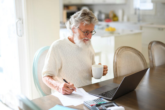 Elderly gentleman thoughtfully reviews his finances at the kitchen table