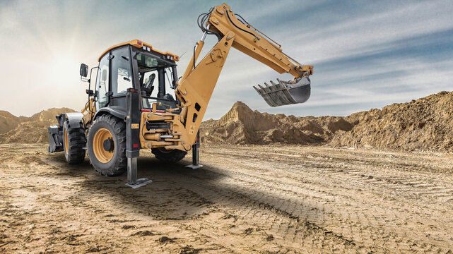 A universal excavator loader is operating on a construction site. The machine is lifting soil with its bucket as the sun shines over the landscape