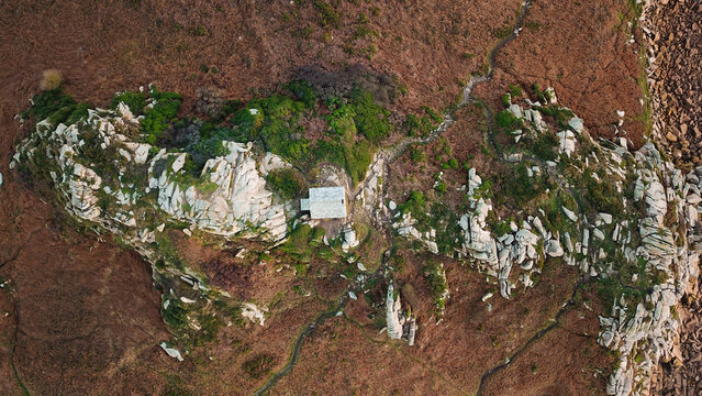 Aerial view of Pointe de Primel featuring rugged granite rock formations, coastal vegetation, and a small stone building nestled on the cliffside in Plougasnou, Bretagne, France.