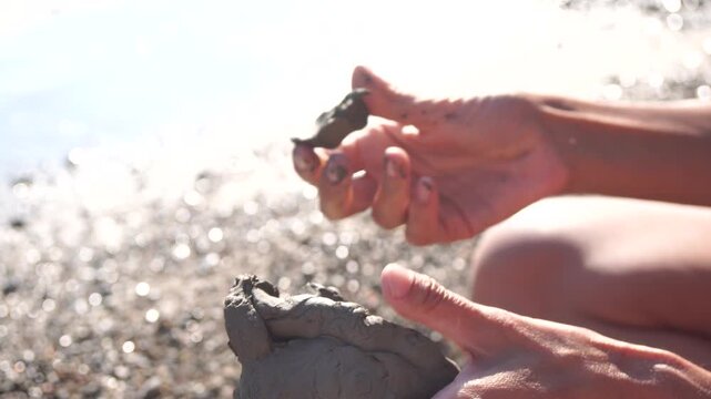 Clay, hands, molding, a person's hands are creating art with wet mud on a sun-drenched pebble beach, a relaxing creative activity