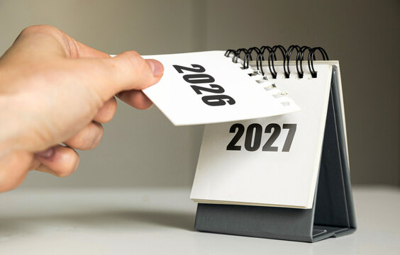 Turning the page from 2026 to 2027 &ndash; New Year calendar concept with hand and desk flip calendar	

