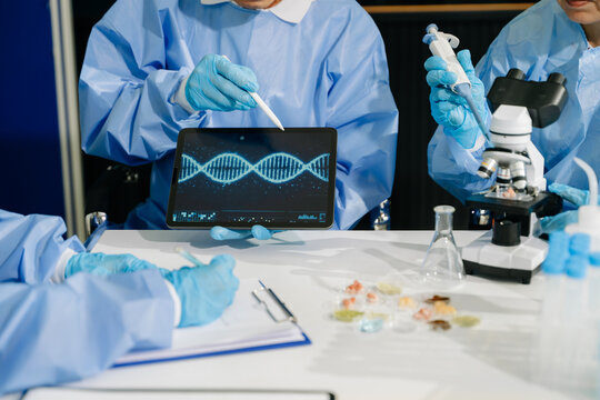 A team of scientists collaborates in a biotechnology lab, using a digital tablet to analyze a DNA helix structure