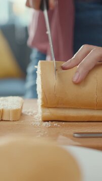 Vertical Screen : Hands Asian woman chef holding knife cutting whole grain bread on wooden board on kitchen table in house. Fresh homemade bread production, Healthy eating traditional bakery concept.