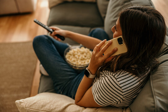 Woman relaxing at home, talking on smartphone, watching tv