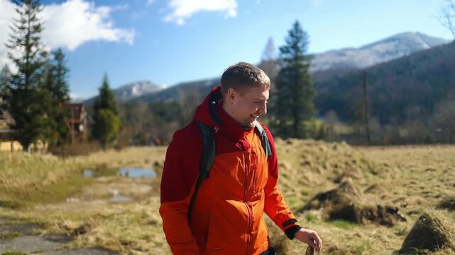 Man in red jacket exploring and interacting with map, in open field with trees mountains in background, with map, backpack, with textile jacket, paper map texture, with red, green accents.