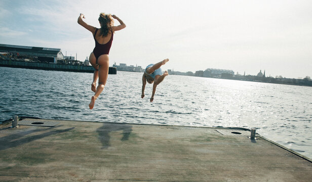 Friends jumping from a dock into water for winter swimming and outdoor fun.