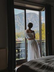 Fototapeta premium Woman in White Dress Gazing Out Window at Mountains