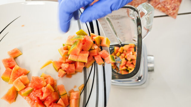 Laboratory technician transferring diced papaya sample into laboratory blender during food analysis and GMO testing preparation