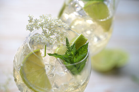 Wine cocktail spritz called Hugo made from prosecco, syrup and soda, garnished with elderflowers, mint leaves and lemon slices in a drinking glass, selected focus