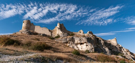 Fototapeta premium Ruins of an ancient stone fortress perched on a hill beneath a clear sunny sky, symbolizing history and exploration.