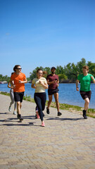 Obraz premium Friends running together along sunny riverside path during fitness workout. Concept of outdoor cardio, running club, active recreation, healthy habits and summer training.