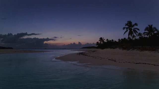 Showing shallow lagoon inlet changing color with daylight fading at tropical beach, with palms