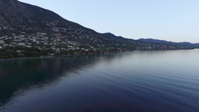 Small Sailboat Anchored Beneath Verga Cliffs Near Kalamata, Greece, Morning Aerial View of Calm Blue Sea, Coastal Village in Mountain Shadow and Peaceful Mediterranean Bay
