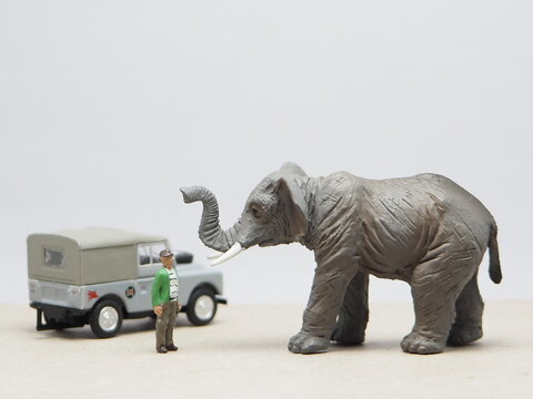 Mini toy of action figure at outdoor with blur background. Miniature photography concept design. Minifigure of zookeeper crew character with elephant animal at zoo. Conservation concept with 4wd car.