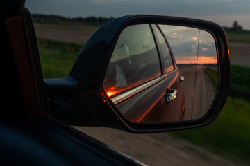 Fototapeta premium Freedom and travel concept with scenic orange sunset clouds reflected in automobile wing mirror on a rural evening way