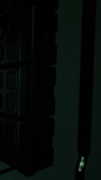 A metal hook is attached to a dark wall next to several storage boxes. The setting appears to be a warehouse or storage area. Light from the side partially illuminates the scene.
