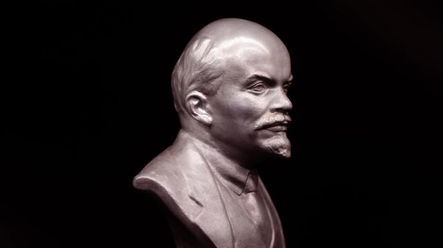 Metal bust of Lenin rotating in dramatic light, historical sculpture close-up