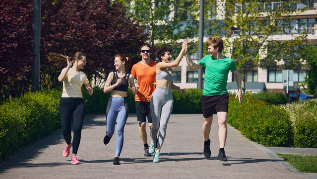 Group of young runners celebrating successful outdoor workout with high five in park. Concept of achievement, teamwork, motivation, active lifestyle, friendship and fitness success.