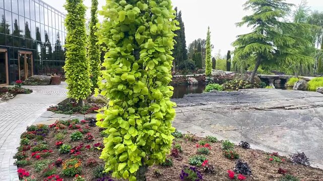 A small waterfall in a beautiful garden with flowers well trimmed trees and a glass house