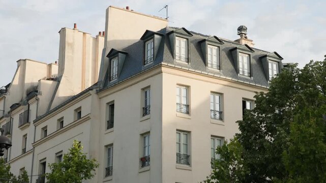 Low-angle architectural view of a classic Parisian Haussmann building corner, showing typical cream stone facades, wrought iron balconies, and a zinc mansard roof with dormer windows camera tilting up