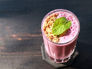 A high-angle shot of a vibrant pink berry smoothie served in a textured glass. The smoothie is topped with a sprinkle of crunchy oat granola and a fresh, bright green mint leaf for a pop of color. © VH_World