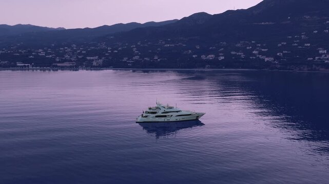 Luxury motor yacht anchored on calm Mediterranean sea near Verga, scenic mountain coastline and coastal village by Kalamata, Greece