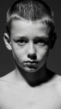 Vertical video: Standing shirtless boy holding still in studio as cam starting recording, top light