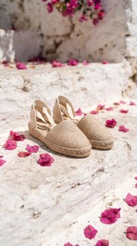 Beige woven espadrille sandals on white stone steps with pink flower petals