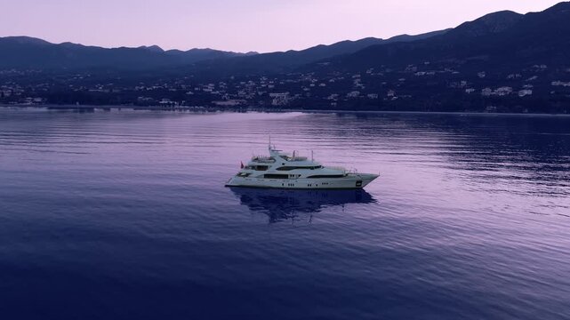 Luxury motor yacht anchored near Verga coast before sunrise, calm Mediterranean sea, mountain village and scenic Kalamata Bay in Greece
