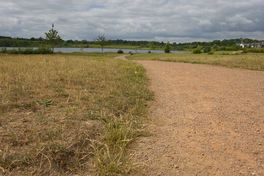 Hampton Water, Peterborough, England, UK - July 01 2026: Beeby's Lake West, Follow the path down to the lake, dramatic cloudy sky, and summer grass.