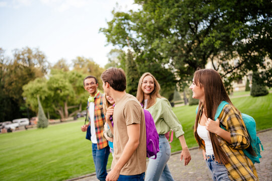 College friends walking on campus together with backpacks smiling and chatting during a sunny day outdoors