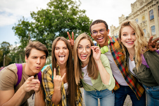 Happy group of young friends laughing and posing outdoors on a college campus, playful students taking a selfie and enjoying time together