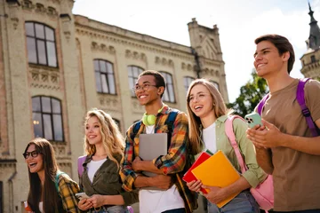 Fototapeten Musik Smiling diverse college students walking outside historic campus with backpacks, notebooks and laptop enjoying friendship and campus life  © deagreez