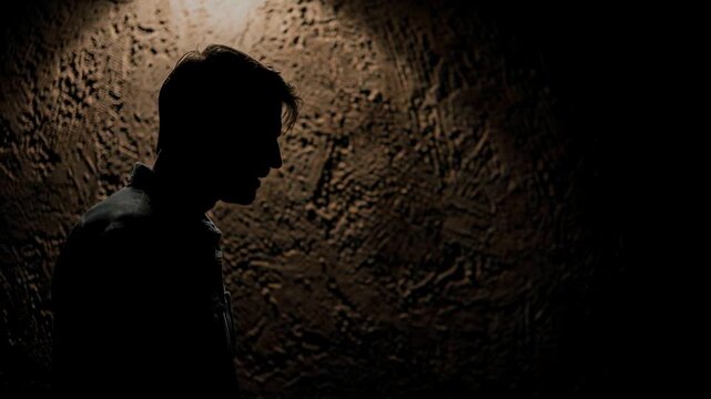 Silhouette of a man standing contemplatively against a textured dark wall with shadow effects