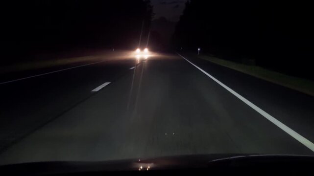 Night highway with oncoming car headlights and wet reflective asphalt under dark sky
