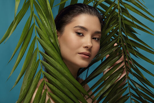 Well groomed woman peeks out from behind palm leaves.