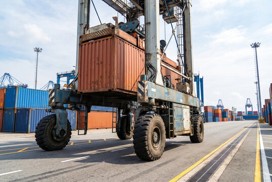 Container terminal straddle carrier lifting cargo in shipping yard  