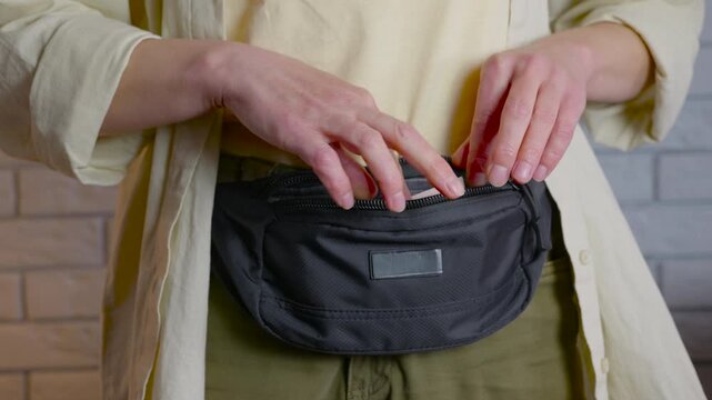 Woman putting cash passport and cards into a fanny pack. Young woman's hands putting cash, including dollars and euros, along with a passport and credit cards, into a convenient black fanny pack