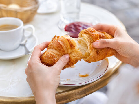 Persona partiendo un croissant de mantequilla reci&eacute;n horneado durante el desayuno.