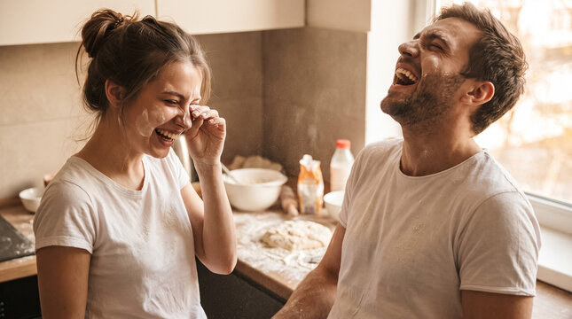 Happy young couple baking together in kitchen, laughing and having playful flour fight for fun at home