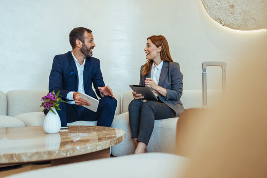 Business Colleagues Discussing Work in Hotel Lobby Lounge With Tablets and Luggage