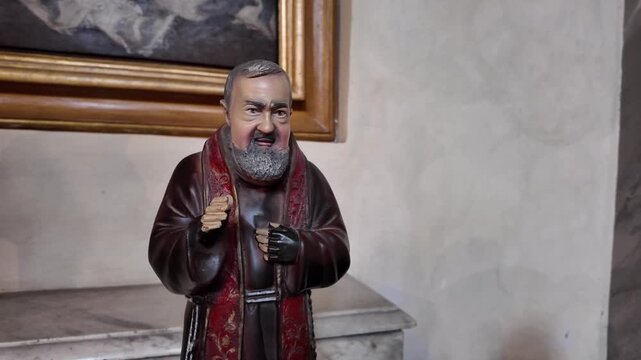 Cinematic View Of A Devotee Praying Before A Bronze Statue Of Padre Pio