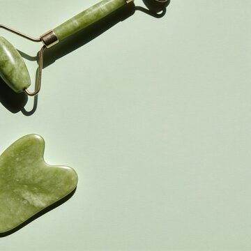 A serene composition featuring a jade facial roller and gua sha tool on a pastel green surface, bathed in soft, diffused light, evoking a sense of tranquility and self-care