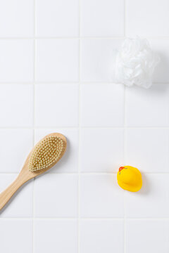 Top view of baby bath product mockup background with yellow rubber ducks. Flat lay of body brush, bath puff, and white towel on square tile wall with copy space for cosmetic display.