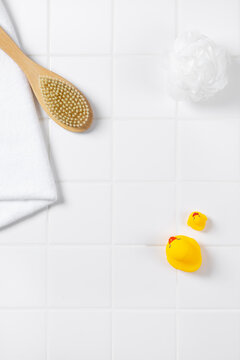 Top view of baby bath product mockup background with yellow rubber ducks. Flat lay of body brush, bath puff, and white towel on square tile wall with copy space for cosmetic display.